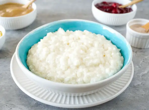 Cremiger Milchreis mit Risottoreis, serviert in einer blauen Schüssel, daneben Apfelmus und Preiselbeeren.