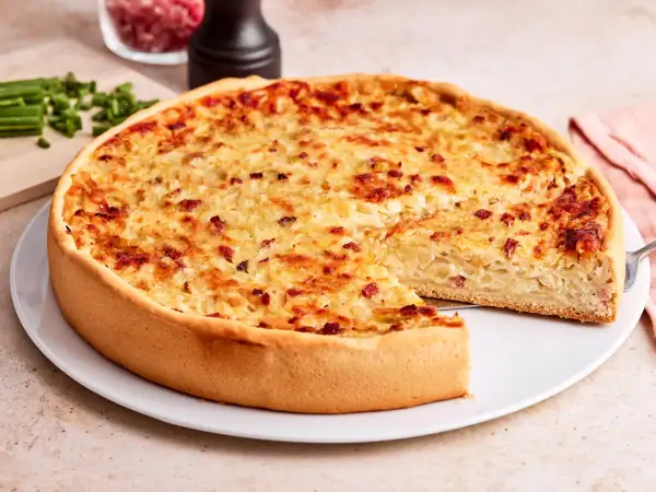 Ein goldbrauner Zwiebelkuchen mit Speck, bereit zum Servieren. Ein Stück fehlt, was Lust auf mehr macht. Perfekt für ein Zwiebelkuchen Rezept.
